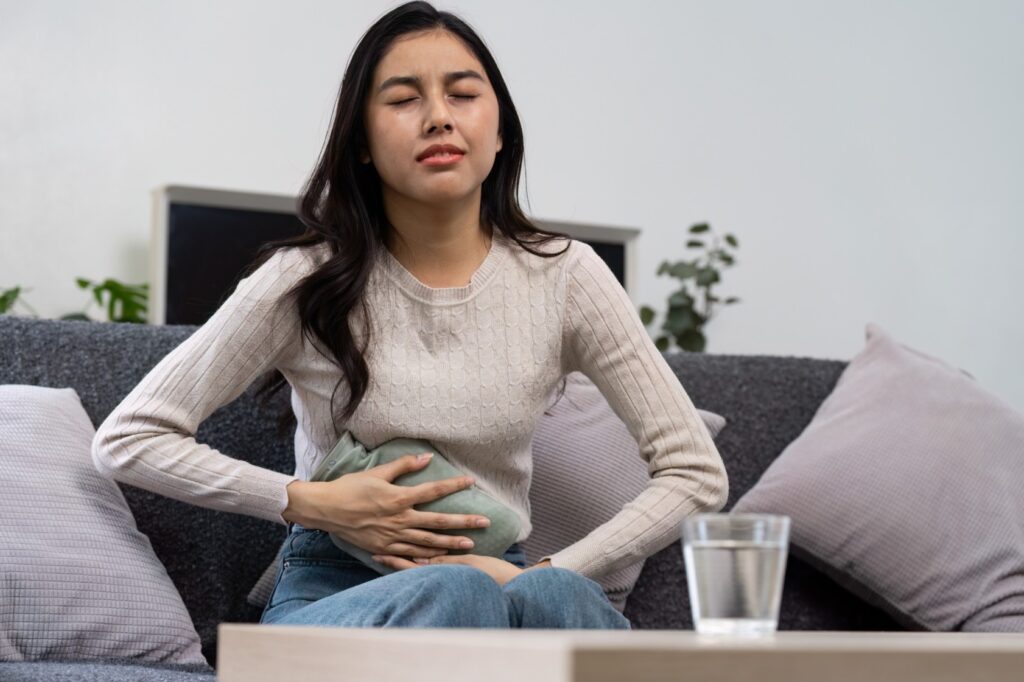 Woman holding hot water bottle soothing stomach discomfort, addressing bloating and digestive concerns.